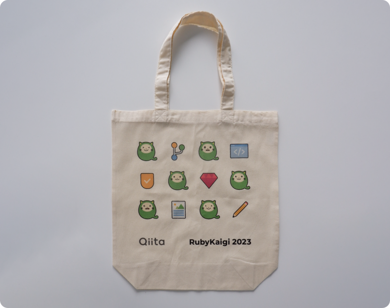 生成のベージュ色のトートバッグに、緑のたぬきのキャラクターであるきーたんとルビーのアイコン、鉛筆やファイルのアイコンが格子状に配置されています。下部にはQiitaのロゴとRubyKaigi 2023のロゴがプリントされています。